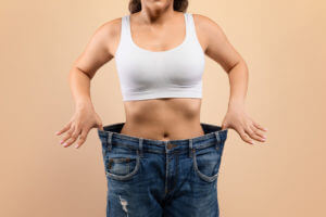 Young female in oversized jeans demonstrating results of her Weight Loss Programs.