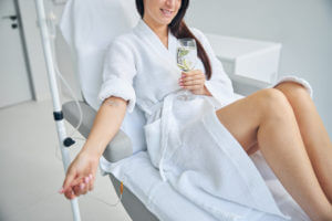 A woman smiling during an IV vitamin infusion therapy for vitamin and fast nutrient absorption.